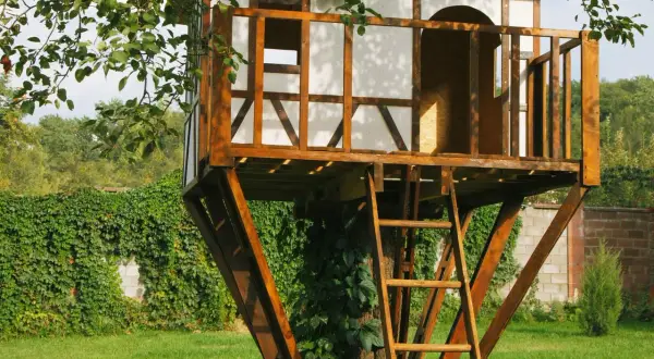 Uroczy projekt domku na drzewie z czerwoną dachuówką i drewnianą drabiną, otoczony zielenią.