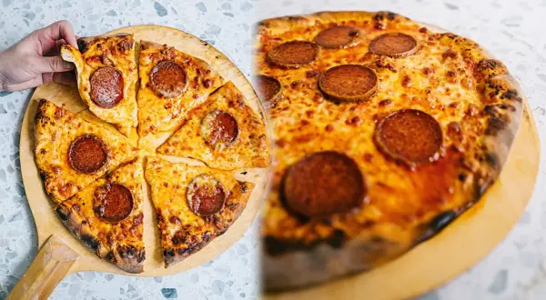 En hand tar en bit av en klassisk neapel pizza med pepperoni och smält ost.