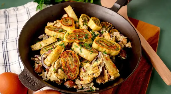 Herzhafte Maultaschen-Pfanne mit Rührei, Zwiebeln und frischen Kräutern, appetitlich in einer Gusseisenpfanne serviert.