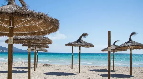 Słomiane parasole na piaszczystej plaży nad turkusową wodą, idealne na wakacje w zatoce alkudyjskiej.