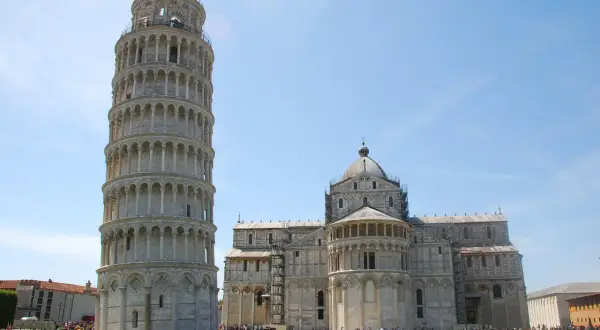 La Torre di Pisa si può salire, con la cattedrale sullo sfondo. Turisti ammirano la celebre struttura pendente sotto un cielo azzurro.