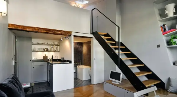 Moderno loft con altillo. Escalera metálica negra, cocina compacta y baño con azulejos. Ideas para espacios pequeños.