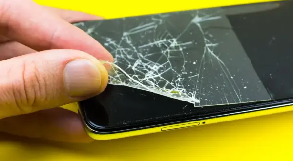 Dłoń zdejmuje pęknięte szkło hartowane 9h z ekranu telefonu.