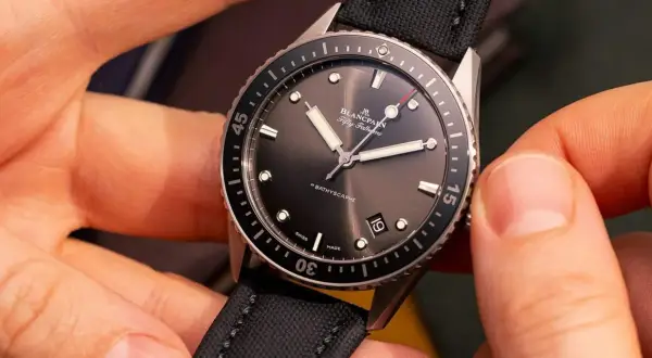 Manos ajustando un reloj automático Blancpain Fifty Fathoms Bathyscaphe con correa de tela negra.