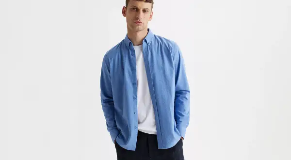 Mężczyzna w niebieskiej koszuli i białej bluzce pod spodem, w kratę spodnie. Idealny zestaw smart casual.