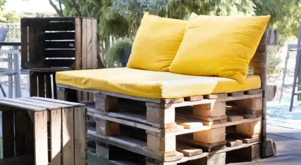 Kanapa z palet i skrzynek, ozdobiona żółtymi poduszkami. To przykład, upcycling co to znaczy: nadawanie drugiego życia przedmiotom.
