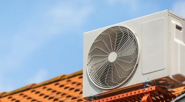 Unité extérieure d'une pompe à chaleur rafraîchissante installée sur un toit en tuiles, sous un ciel bleu clair.