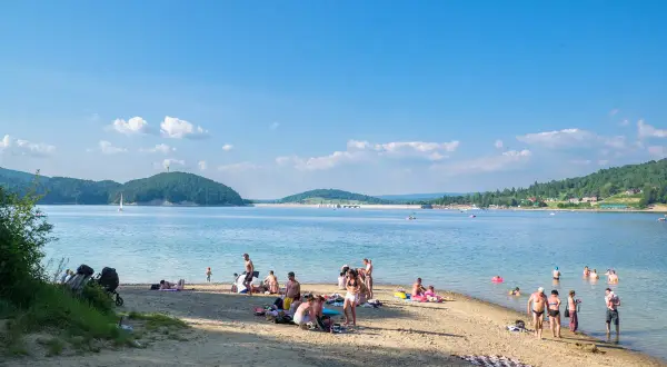 Słoneczny dzień na plaży w Polańczyku-zdroju. Ludzie odpoczywają nad wodą, niektórzy kąpią się, inni opalają.