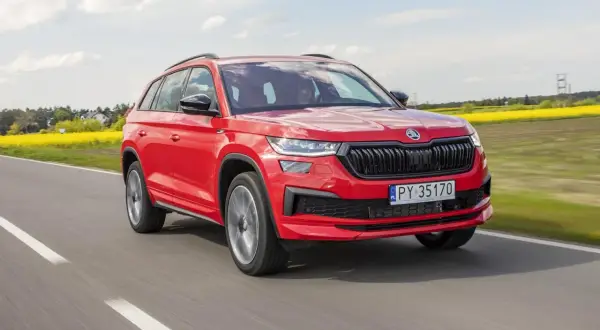Czerwony Skoda Kodiaq 2023 pędzi po drodze, mijając kwitnące pola rzepaku.