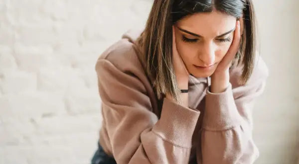 Een jonge vrouw met haar handen tegen haar slapen, diep in gedachten verzonken. Ze lijkt te worstelen met de gevolgen van gaslighting door vrouwen, haar blik neergeslagen.
