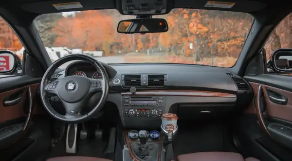 Wnętrze BMW z brązową tapicerką, kierownicą i panelem. Na desce rozdzielczej kubek kawy. Idealne miejsce na podpisanie umowy sprzedaży samochodu.