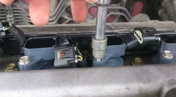 Naprawa Opla z błędem dtc p0301. Mechanik dokręca cewkę zapłonową kluczem nasadowym.