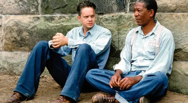 Skazani na Shawshank obsada: Tim Robbins i Morgan Freeman siedzą przy kamiennym murze, w więziennych strojach.