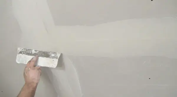 Hand verspachtelt Rigipsplatten mit einem Spachtel. Die Naht wird geglättet, um eine ebene Oberfläche für die weitere Bearbeitung zu schaffen.