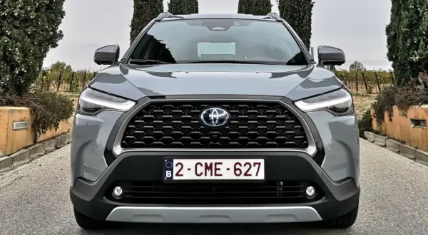 Szary SUV Toyota Hybryda 2022 z przodu, z grillem i światłami LED, na tle winnicy i drzew.