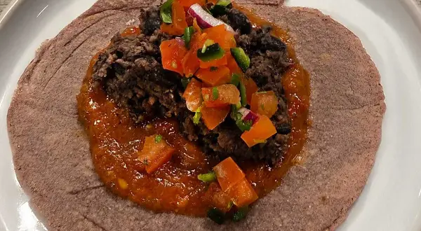 En lila tortilla med en klick refried beans, toppad med salsa och hackad lök.