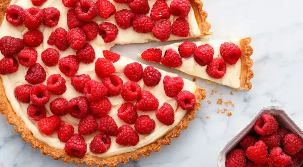 Pyszna tarta z malinami, z kremowym nadzieniem i chrupiącym spodem, ozdobiona świeżymi malinami.