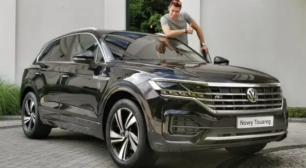 Mężczyzna z kciukiem w górę przy nowym, czarnym Volkswagenie Touareg. Jego imponujące wymiary robią wrażenie.