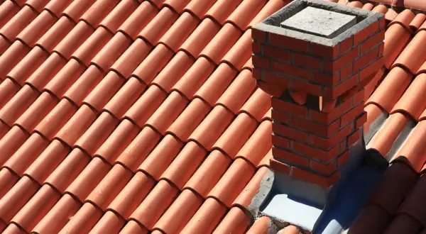Ceglany komin na dachu z dachówki. Dowiedz się, jak uszczelnić komin w mieszkaniu, by uniknąć przecieków.