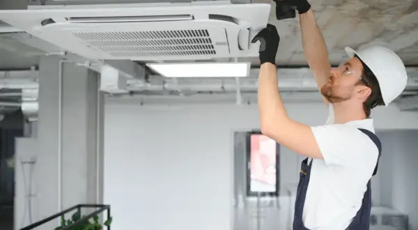 Technik w kasku montuje klimatyzator kasetonowy na suficie.