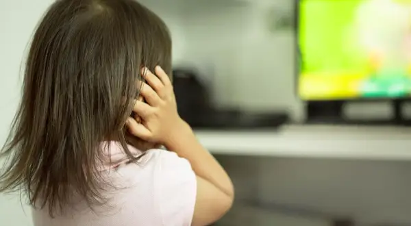 Dziewczynka z autyzmem zasłania uszy, reagując na bodźce. Ekran telewizora emituje jasne, intensywne kolory.