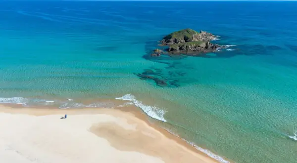 Pusta plaża na Costa Smeralda, z turkusową wodą i samotną postacią spacerującą brzegiem.