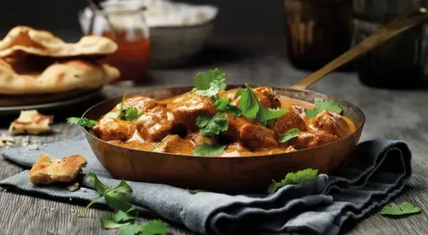En skål med krämig tikka masala, toppad med färsk koriander, serveras med naanbröd och ris.