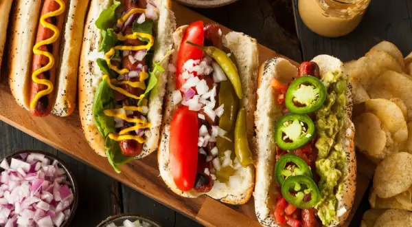 Cztery pyszne hot dogi z różnymi dodatkami: musztarda, cebula, pomidor, papryczki i guacamole.