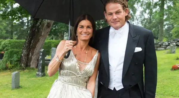 Sian Persson och hennes man, klädda för fest, delar ett paraply i regnet.