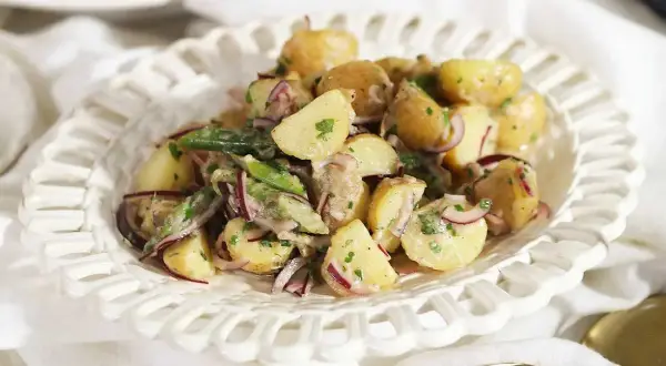 En krämig potatissallad med rödlök och örter, ser ut att vara den godaste potatissalladen för en sommarbuffé.