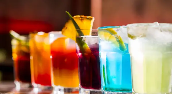 Kolorowe drinki na barze, w tym niebieski koktajl z plasterkiem cytryny, przypominają letnie orzeźwienie, jak Bacardi Razz drink.