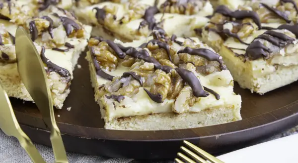 Ein Stück "friss dich dumm Kuchen" mit Walnüssen und Schokoladenglasur auf einem Holzteller, daneben goldenes Besteck.