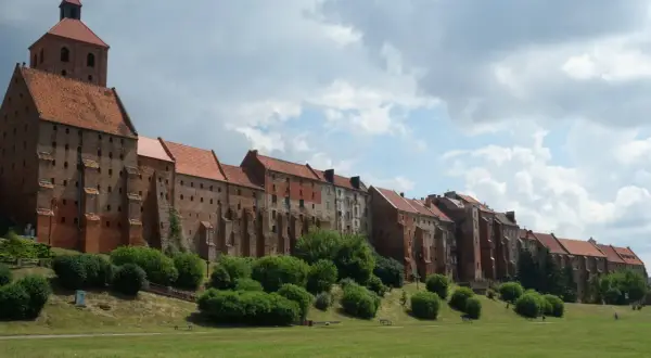Grudziądz atrakcje: imponująca ceglana twierdza z wieżą i dachem z dachówki, otoczona zielenią i trawnikiem.