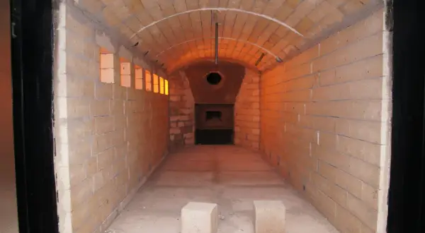 Wnętrze krematorium z ceglanymi ścianami i łukowym sufitem, oświetlone pomarańczowym blaskiem.