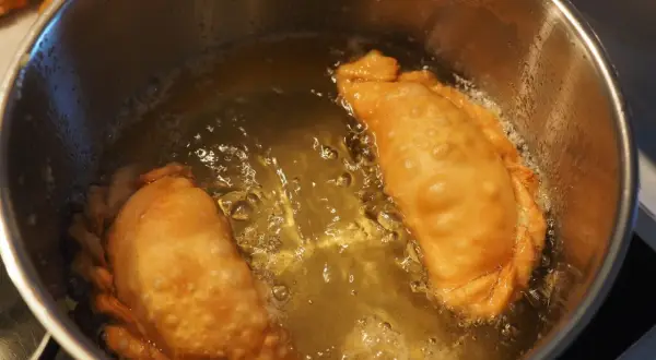 Due calzoni dorati friggono in olio bollente. Si puo friggere con olio d'oliva per un sapore autentico.