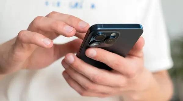 Dłonie trzymające ciemny iPhone, na którym można sprawdzić numer IMEI.