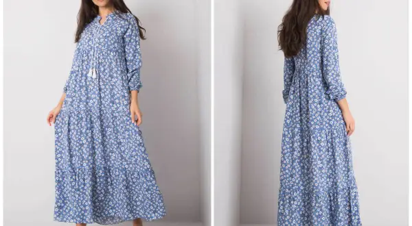 Modelka prezentuje zwiewną, błękitną sukienkę w drobne kwiatki, idealną dla kobiet plus size. Długi fason i falbany dodają jej lekkości.