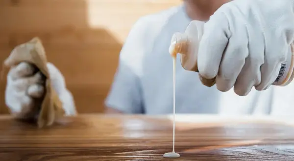 Application d'un produit sur un bois, peut-être pour effacer une tache blanche laissée par un plat chaud.