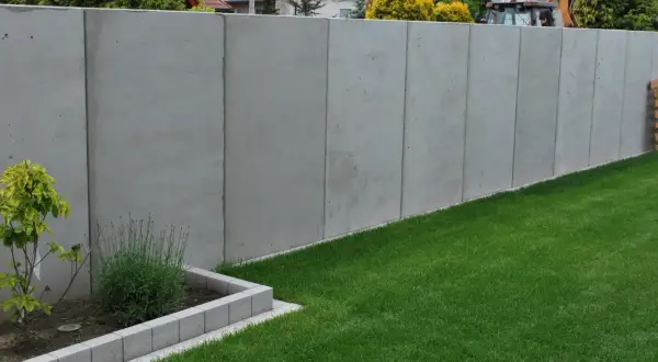 Nowy, wysoki betonowy płot dzieli działki, symbolizując konflikt z sąsiadem o ogrodzenie.