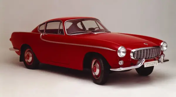 Une élégante Volvo rouge, un modèle emblématique des années 50, se dresse fièrement sur un fond neutre.