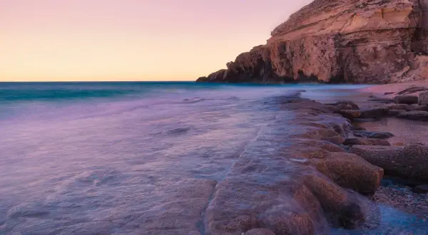 El mar acaricia las rocas de la cala el corral carboneras al atardecer, creando un paisaje sereno y etéreo.