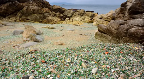 La praia dos cristais, una playa de guijarros de vidrio pulido por el mar, rodeada de rocas y con el océano al fondo.