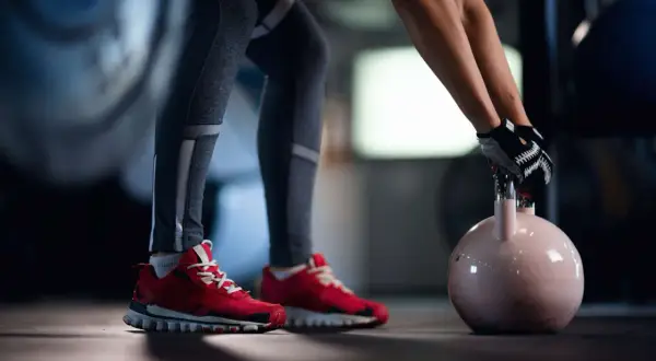 Person mit roten Schuhen und Trainingshandschuhen hebt abends eine Kettlebell für das Krafttraining.