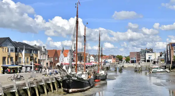 Tre segelfartyg ligger vid kaj i Husum, Tyskland. Bakom dem syns en rad hus och en bro över kanalen.