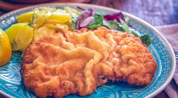 Ein knuspriges Wiener Schnitzel mit Kartoffelsalat und Zitrone auf einem blauen Teller.