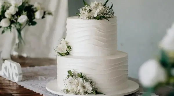 Elegancki tort komunijny, idealny na 20 osób. Białe kwiaty zdobią dwupoziomowe ciasto.