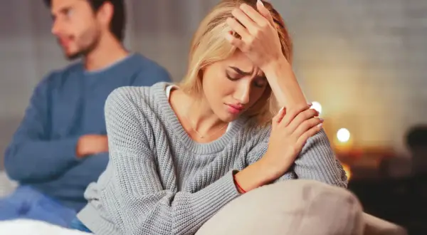 Una mujer angustiada en primer plano, con un hombre de espaldas en el fondo. La escena evoca la confusión y el dolor que a veces acompañan a **que es la limerencia**.