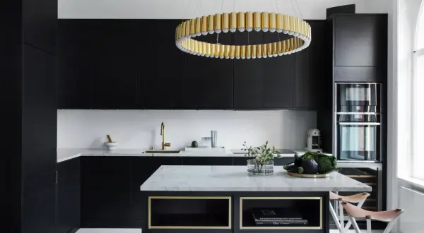 Cucina nera con pareti bianche, isola in marmo, lampadario dorato e sgabelli in pelle.