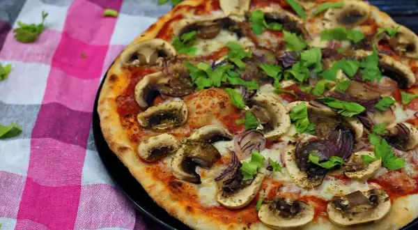 Pyszna pizza z pieczarkami na pizze, cebulą i świeżą natką pietruszki, podana na kraciastej serwetce.