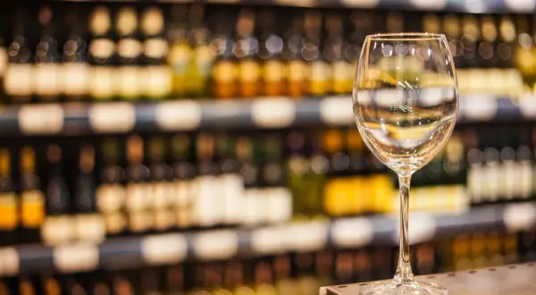 Verre à vin vide sur un comptoir, devant des étagères remplies de bouteilles. L'ambiance évoque une dégustation de vin à Paris.